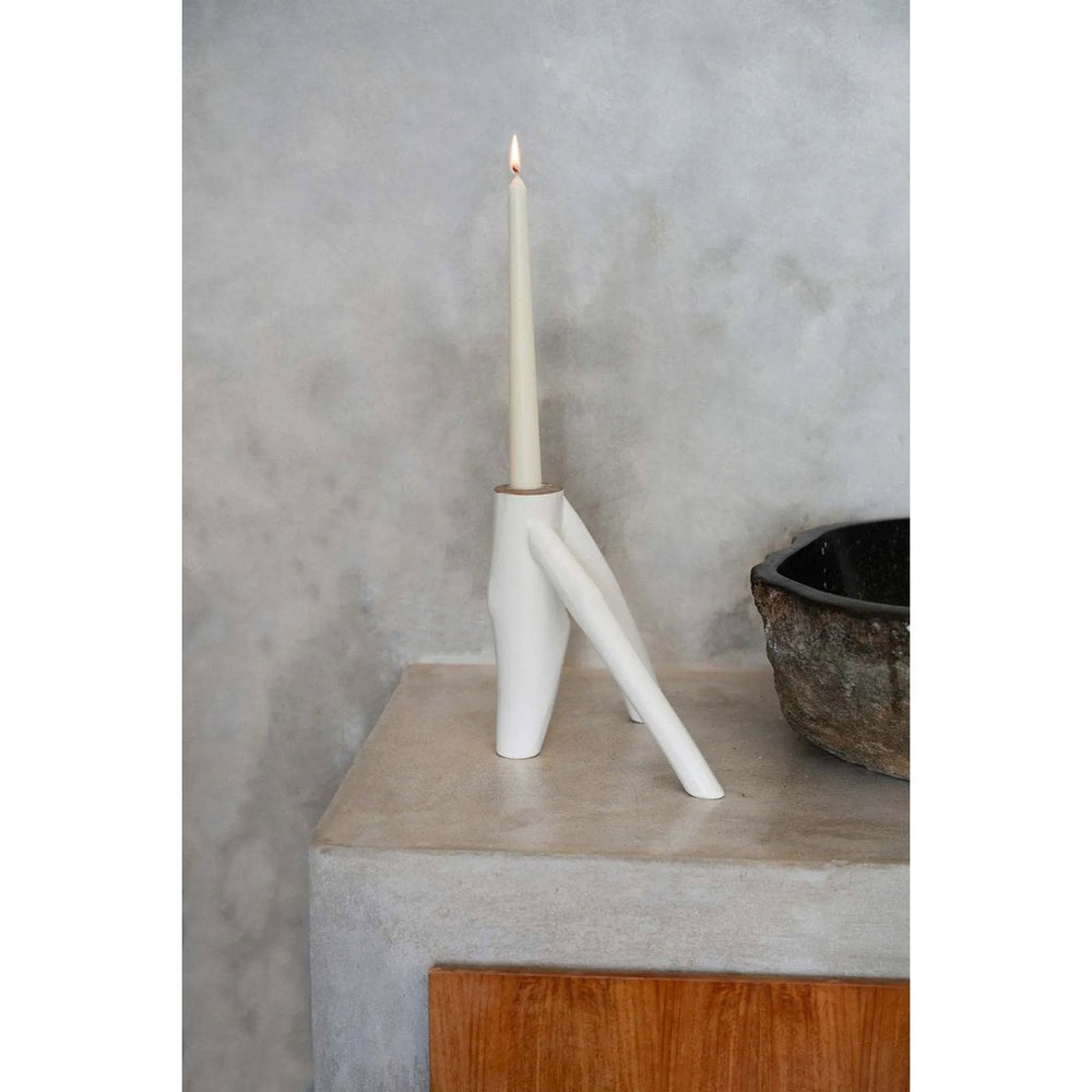 White candle holder with a lit candle on a concrete surface against a gray wall.