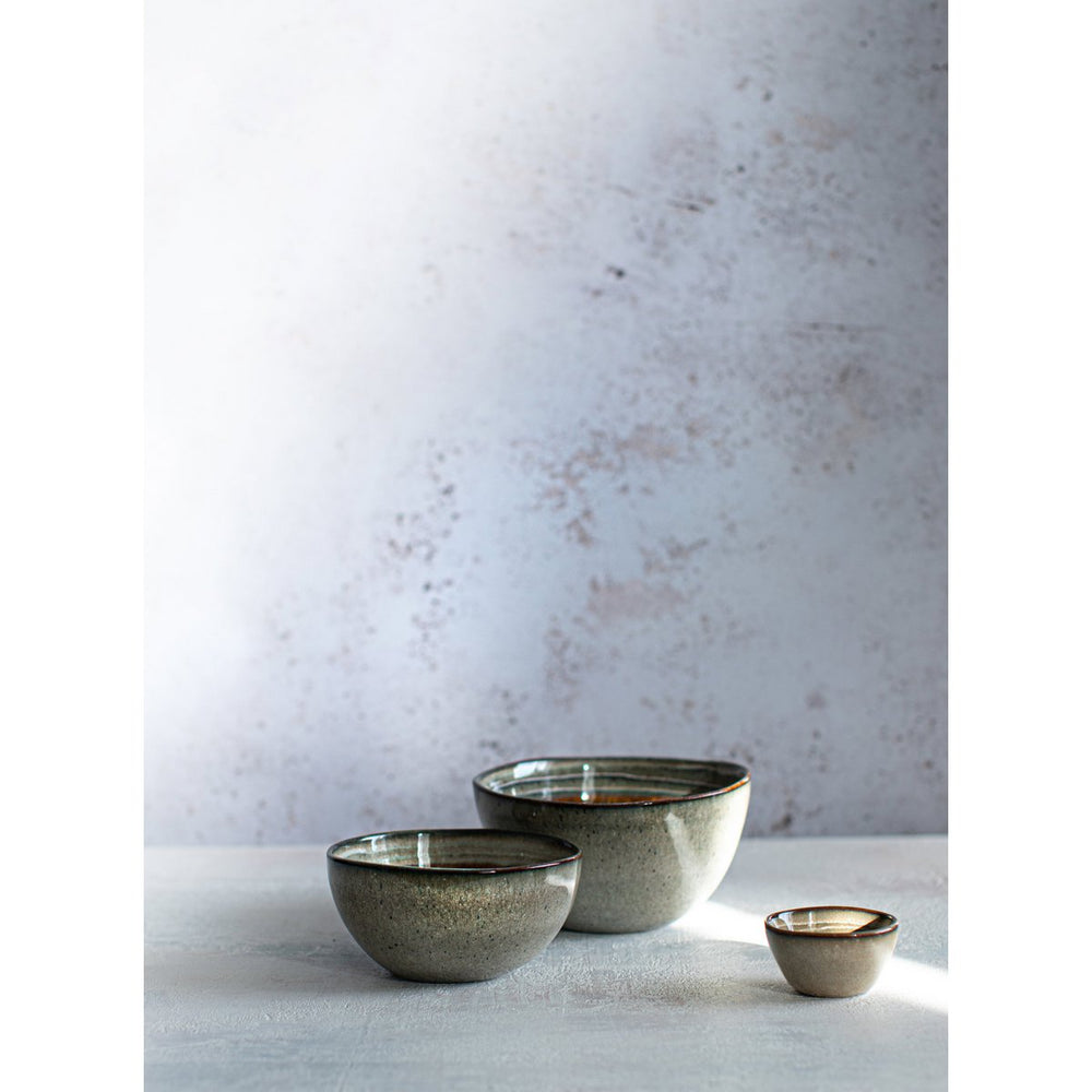 Three ceramic bowls of varying sizes on a light surface with a textured white wall background.
