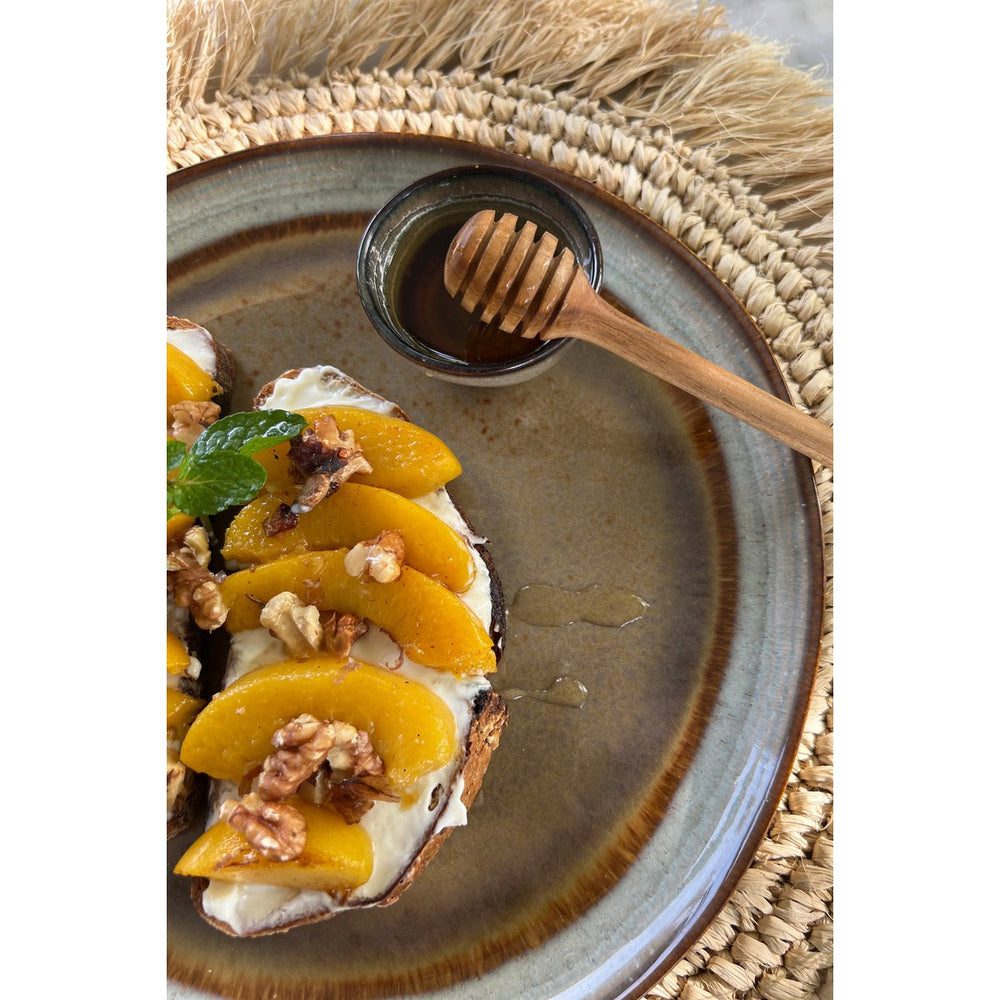 Plated dessert with peaches, cream, and nuts on a rustic plate with a honey dipper.