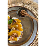 Plated dessert with peaches, cream, and nuts on a rustic plate with a honey dipper.