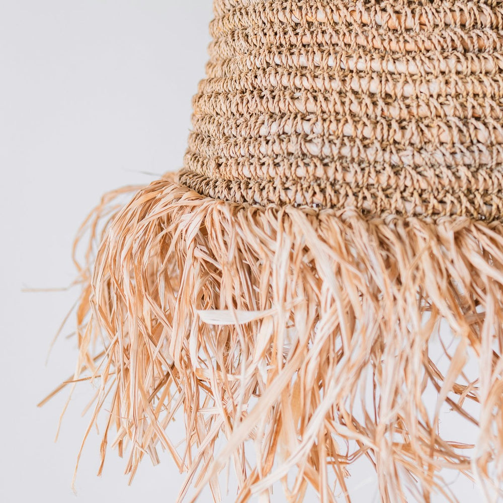 Close-up of a woven straw hat with fringes on a light background