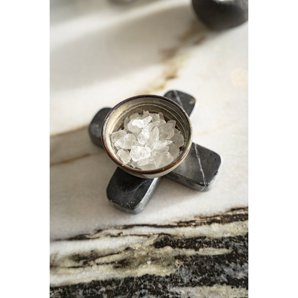 Decorative stone with a small container of crystals on a marble surface