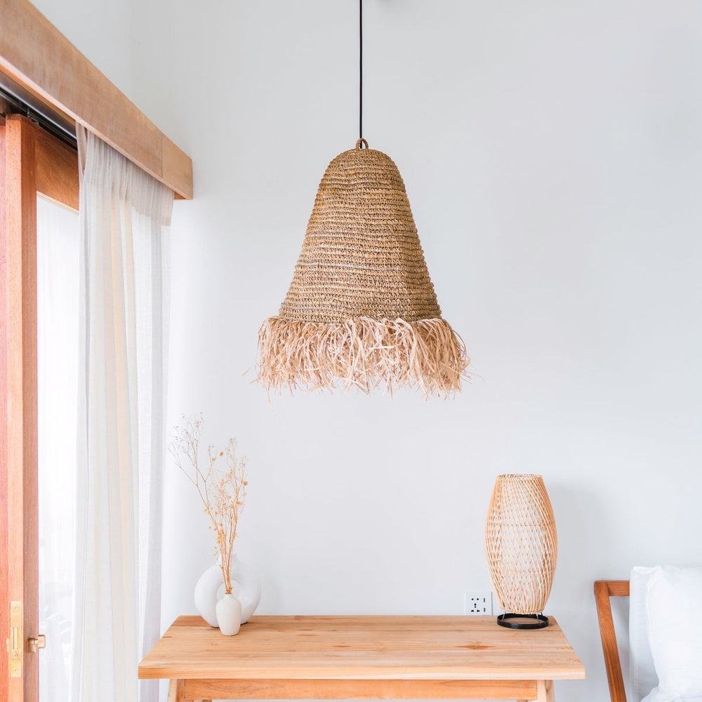 Woven pendant light hanging above a wooden table with a matching lamp on a white wall.